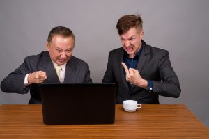 Studio shot of mature Asian businessman and young Scandinavian businessman against gray background diverse yell angry fuck scream frustrated