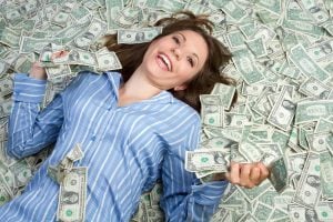 Woman in blue shirt smiling while lying in money