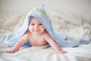 Cute little baby boy, relaxing in bed after bath, smiling happily