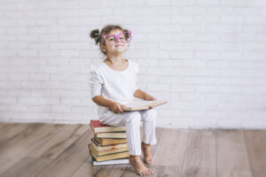 Child little girl sitting on a stack of books with glasses
