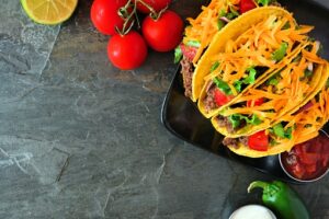 Hard shelled tacos with ground beef, vegetables and cheese, border on a dark background
