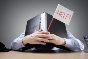 A businessman buries his head under a laptop and asks for help