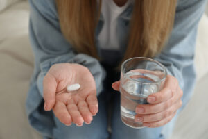 Young woman with abortion pill and glass of water on blurred background, closeup