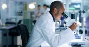 Research scientist analyzing a sample, looking into a microscope, conducting an experiment. Male biologist or chemist working on a futuristic medical development in a laboratory.