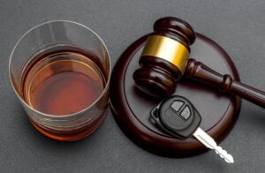 Judge’s gavel with car key and glass of whiskey on black.