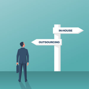 Outsource or inhouse – signpost. Businessman in front of a road sign.