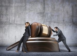 Man And Woman Pushing In Opposite Directions Against Large Gavel