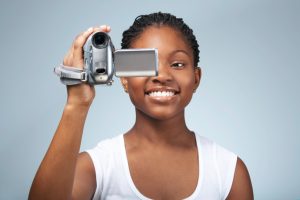 Teenage girl (15-17) using video camera, smiling, close-up