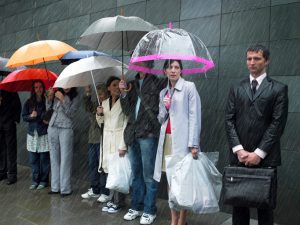 Soaked businessman standing beside group of people under umbrellas