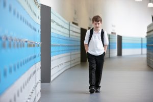 Unhappy schoolboy walking alone in school corridor
