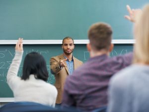 professor teacher at blackboard chalkboard students raising hands
