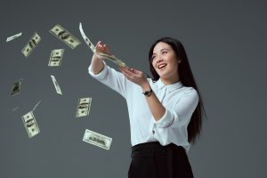 money smiling asian girl throwing dollar banknotes isolated on grey