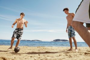 summer associates men playing soccer at beach