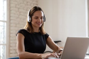 Woman wearing headphones working typing on notebook enjoy e-learning process