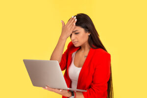 Regrets wrong doing while working online. Sad woman, slapping hand on head having duh moment while looking holding laptop computer