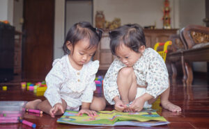 Cute Asian siblings toddler girl playing together at home, Sisters playing with crafts book with sticker at home, Indoor activities for little kids concept