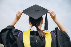 Rear view of young student wearing graduation gown with graduation cap in her commencement day.